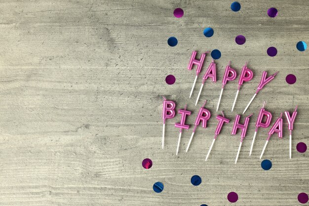 Happy birthday candles and glitter on gray wooden background
