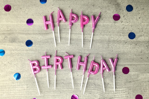 Happy birthday candles and glitter on gray wooden background