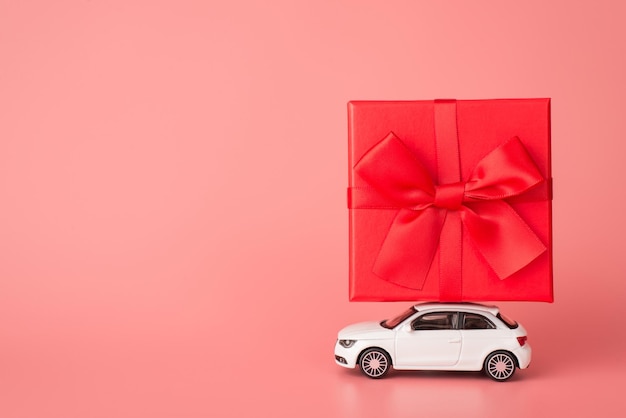 Foto buon compleanno concetto. foto di vista del profilo laterale di una mini auto moderna che trasporta un'enorme confezione regalo di grandi dimensioni sul tetto superiore isolato su uno sfondo rosa chiaro