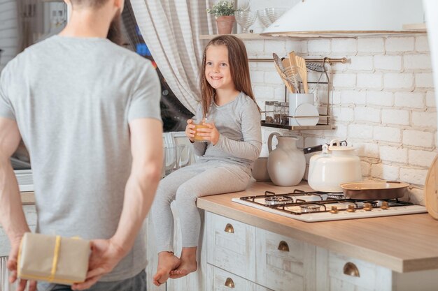 happy birthday girl loving father prepared surprise gift for his little daughter smiling kid sitting in kitchen with glass of juice