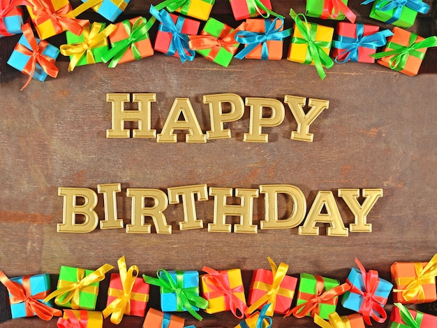 Happy birthday golden text and colorful gifts on a wooden background