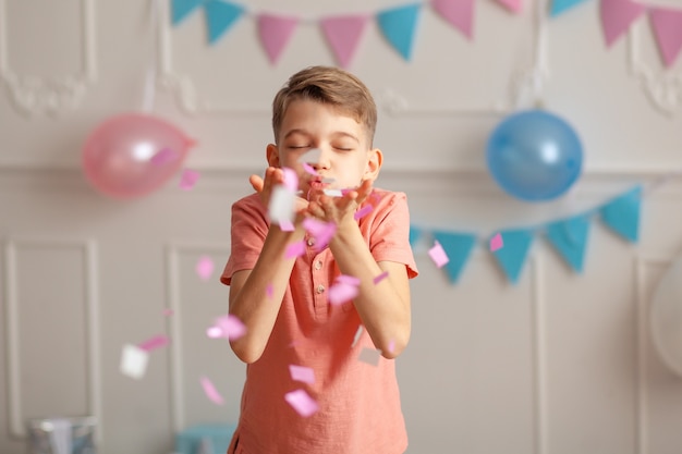 Happy Birthday Portrait of a happy cute boy of 8-9 years old in a festive decor with confetti and gifts.