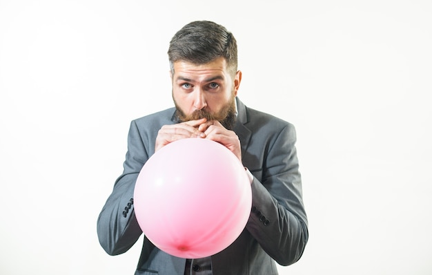 Happy birthday, preparation to party, celebration - attractive businessman with beard and mustache is blowing pink balloon. Stylish man in suit inflating balloon. Handsome bearded man hold air balloon