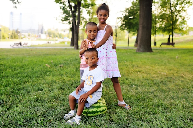 Happy black African American kids playing with a big watermelon in the Park on the grass and smiling.