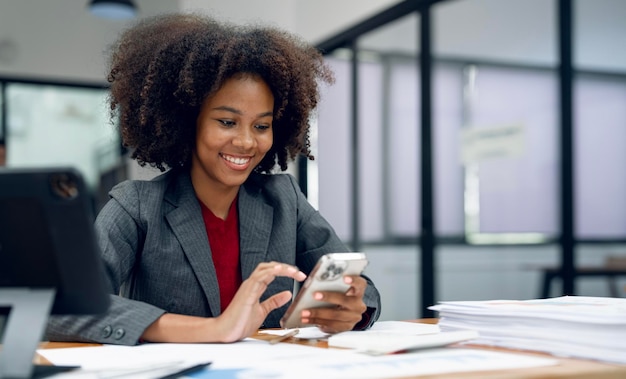 Happy Black businesswoman smiling while reading a text message on mobile phone sitting in an office