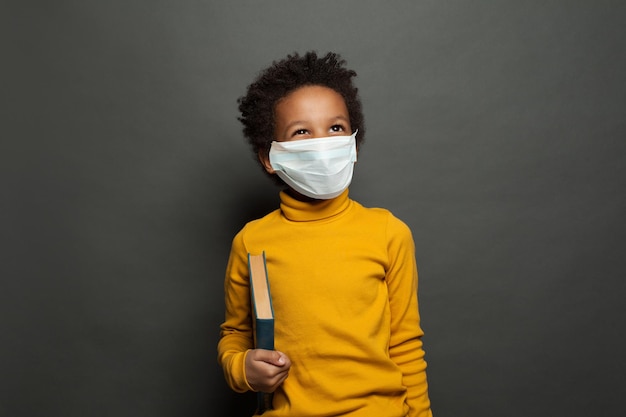 Happy black child boy in medical protective face mask on blackboard background