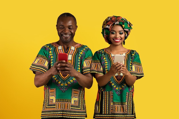 Happy black couple in african costumes using smartphones