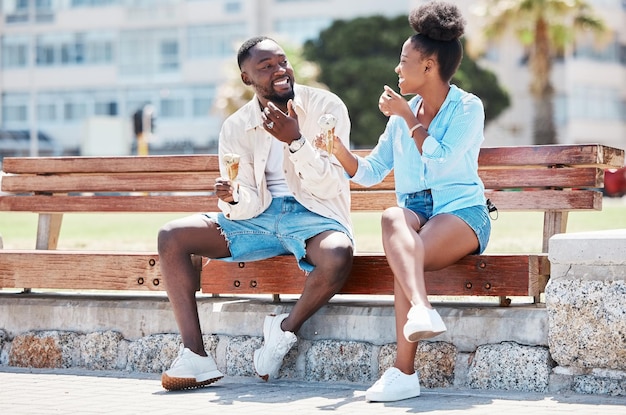 Happy black couple eating ice cream on a beach bench together smiling while bonding and laughing Young African American man and woman enjoying their summer romance free time and relationship