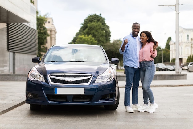 Happy black couple leaning on new car showing auto keys