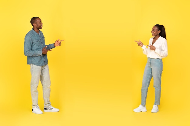 Photo happy black couple pointing fingers at each other yellow background