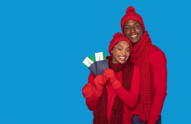 Happy black couple in red scarves holding tickets blue background