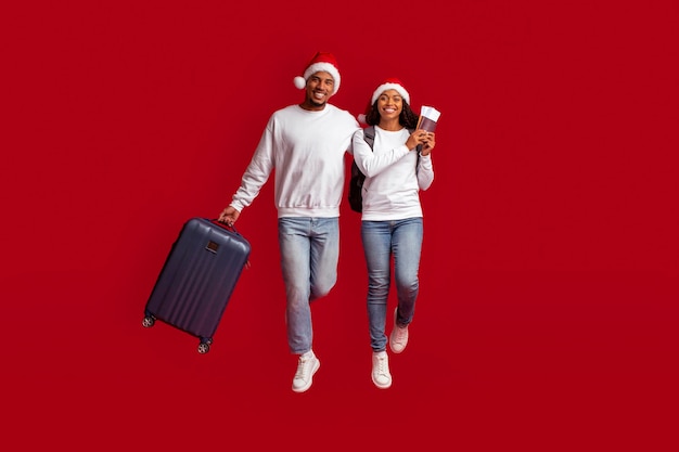 Happy black couple in Santa hats holding passport tickets