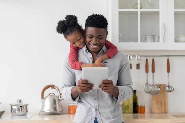 Happy black father and daughter using pad together at home