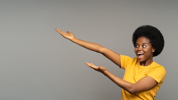 Happy black girl point aside up holding open palms presenting product advertising or sale at studio