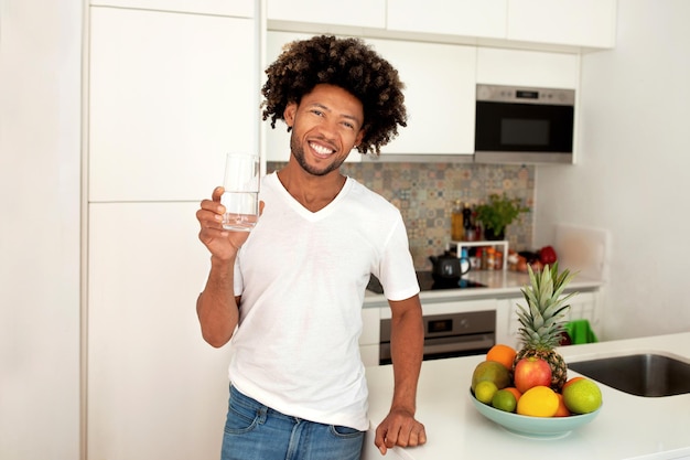 Happy black guy holding glass of water in modern kitchen