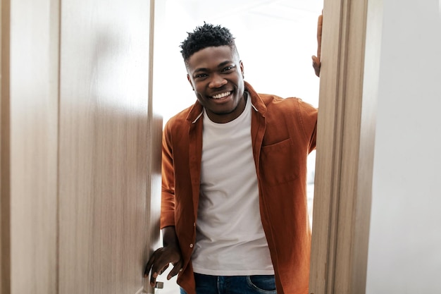 Photo happy black guy opening door of his apartment standing indoor