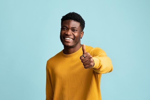 Happy black guy showing thumb up posing on blue background