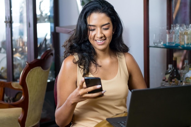 happy black haired latin woman chatting with her smartphone from her living room