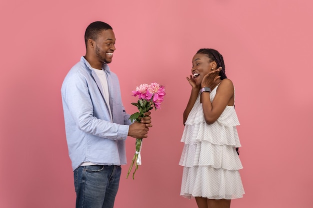 Happy black man making surprise for woman giving flowers