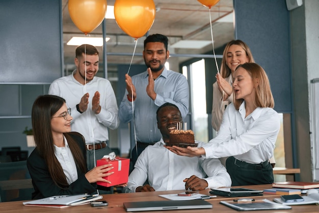 Photo happy black man with sweet cake with candles employee having a birthday in the office group of workers