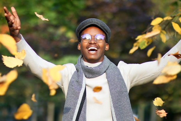 Happy black man young african afro american guy having fun in golden autumn park with leaves at fall