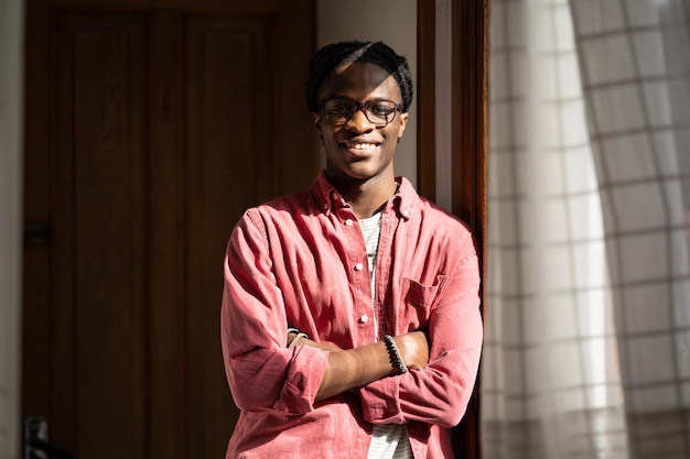 Happy black millennial student guy standing in sunny room smiling at camera enjoying dorm life