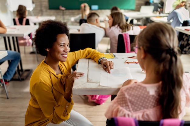 Happy black teacher assisting her student during a class at elementary school