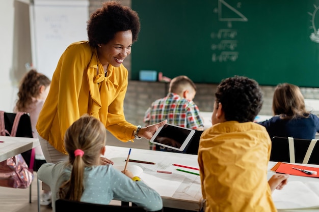 Happy black teacher and elementary students using digital tablet in the classroom