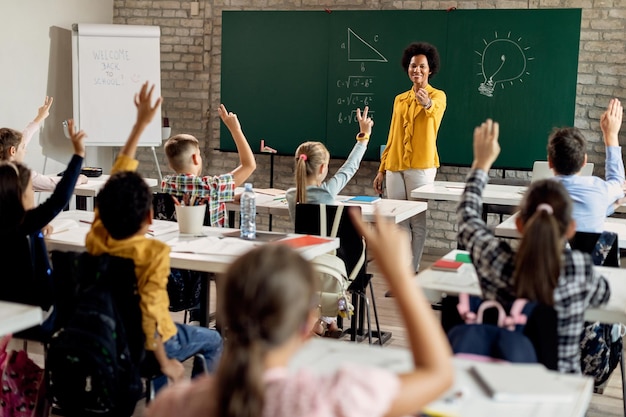 사진 수업 중 질문에 답하기 위해 손을 들고 있는 초등학생들을 가리키는 행복한 흑인 교사