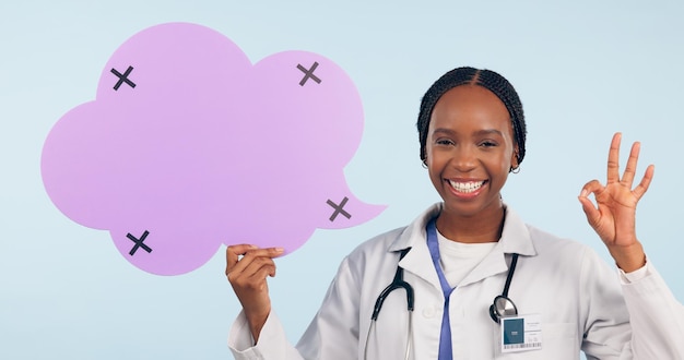 Happy black woman doctor and ok sign with speech bubble for social media review against a studio background portrait of african female person surgeon or nurse showing icon okay or emoji on mockup