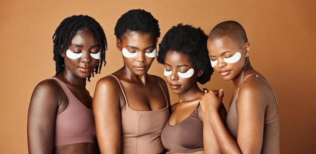 Happy black woman eye patches and skincare for beauty epilation or anti aging against a brown studio background Group portrait of African female people or model in dermatology health and wellness