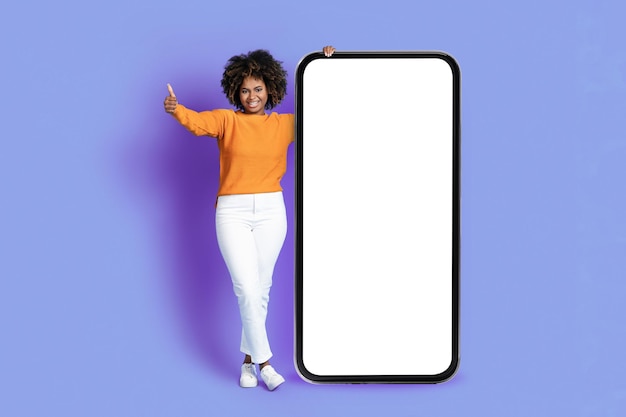 Happy black woman posing with big phone showing thumb up
