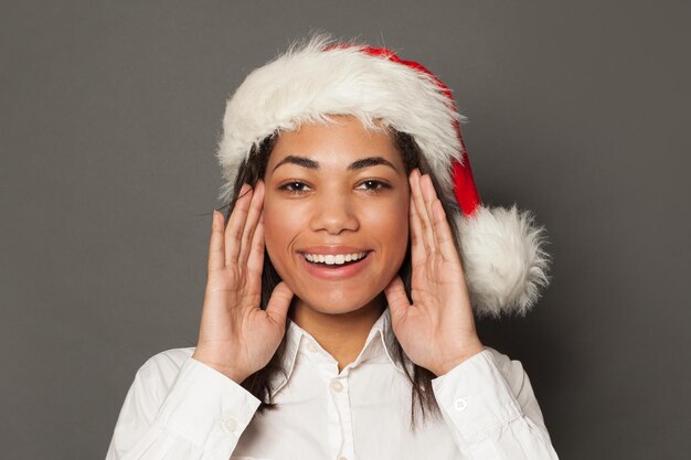 Happy black woman in Santa hat on gray background