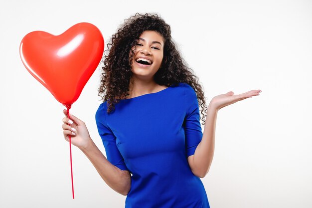 Happy black woman with red heart shaped balloon wearing blue dress isolated