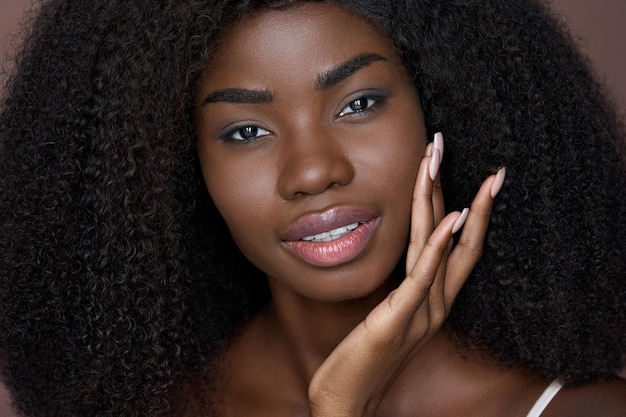 Happy black young woman touching flawless face skin on brown background