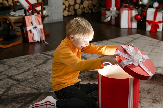 幸せな金髪の少年は、家で子供の休日のための内側から光る大きなギフト ボックスに見えるクリスマス プレゼント