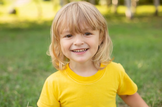 Счастливый блондин сидит на лужайке в желтой футболке с зубастой улыбкой