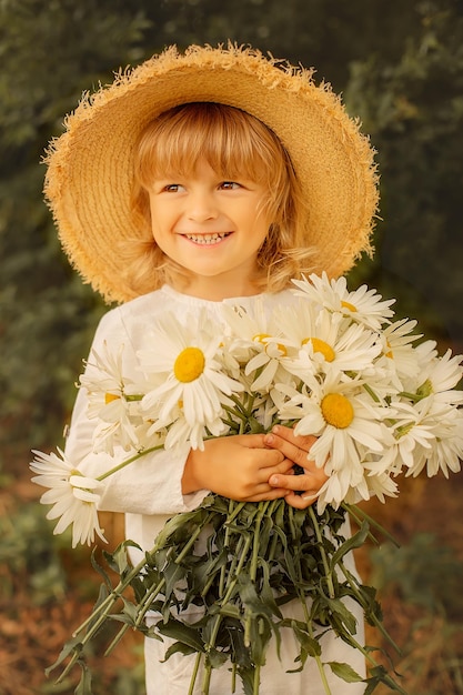 happy blond boy in a white linen suit straw hat and daisies in his hands