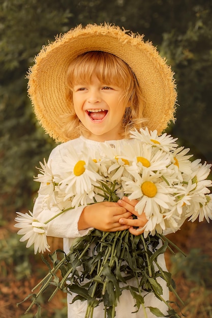 happy blond boy in a white linen suit straw hat and daisies in his hands