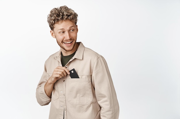 Happy blond guy put credit card in his pocket smiling and looking behind at empty space promo text concept of shopping and money
