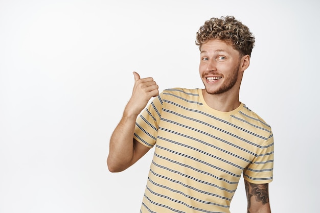 Happy blond hipster guy showing advertisement behind pointing left and smiling recommending click on link checking out store banner white background