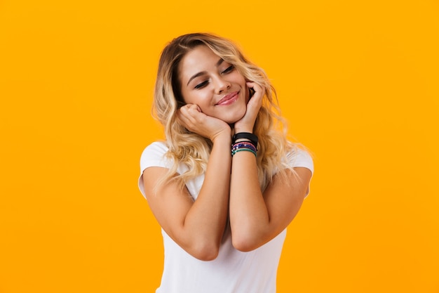 Happy blond woman in basic clothing smiling and looking at you, isolated over yellow wall