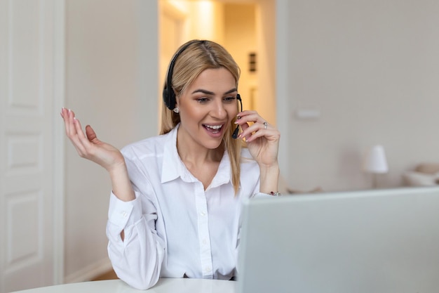 Happy blond woman wearing headphones and microphone looking at\
webcam smiling at camera laughing during virtual meeting or video\
call talk employee working from home screen view head shot