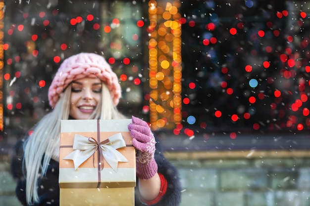 Happy blond woman wears knitted pink hat enjoying gift at the winter fair. Space for text