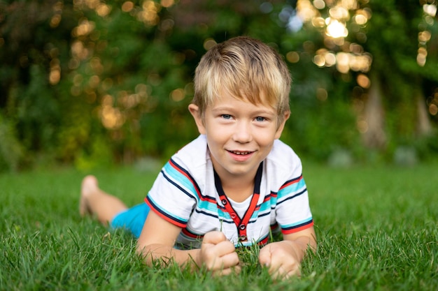 Happy blonde baby with blue eyes lies on the grass looks at the camera smiles outdoor recreation holidays