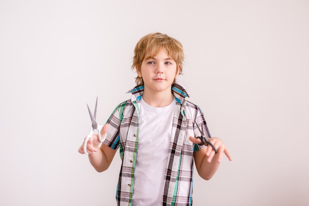 Happy blonde boy European appearance in a white shirt holding scissors