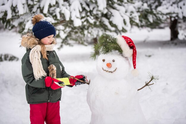 Happy blonde cute child girl plaing with a snowman