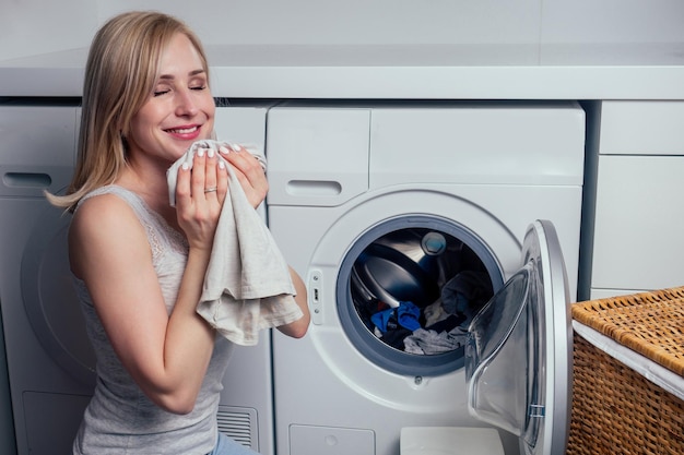 Happy blonde female washing clothes feeling happy about soft fresh laundry aroma fabric softener aromatherapy