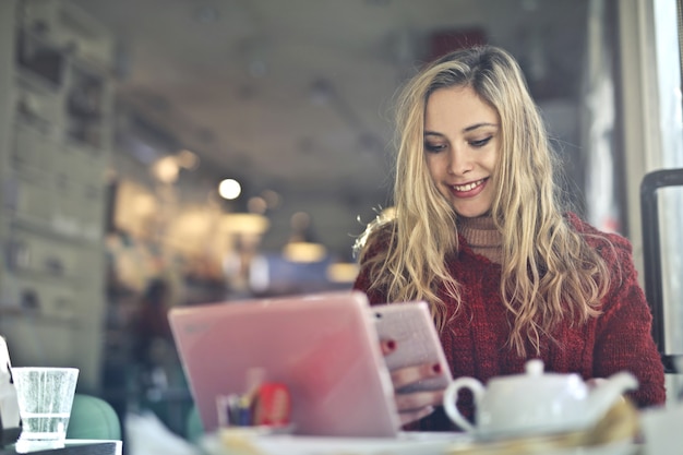 Ragazza bionda felice in una caffetteria con il suo computer portatile