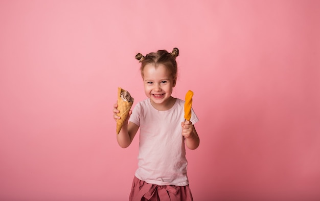 Happy blonde girl holds two ice creams on a pink surface with space for text